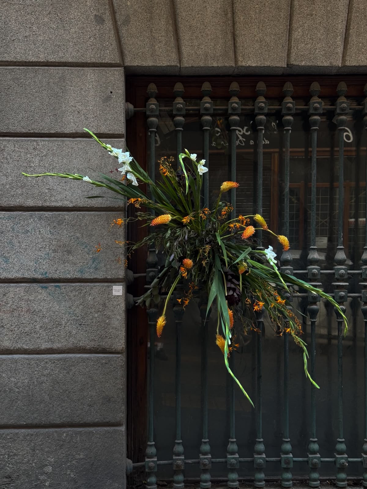 Intervención floral verde, blanca y naranja sobre una reja en Madrid