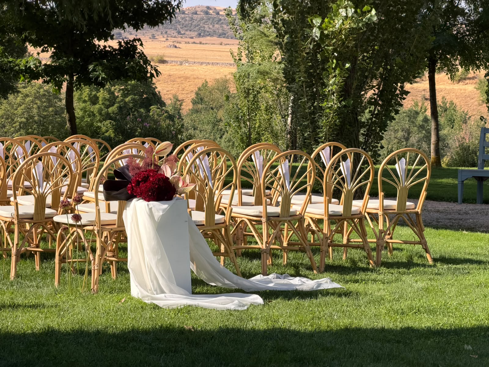 Ceremonia de boda al aire libre con sillas de madera y una composición floral burdeos