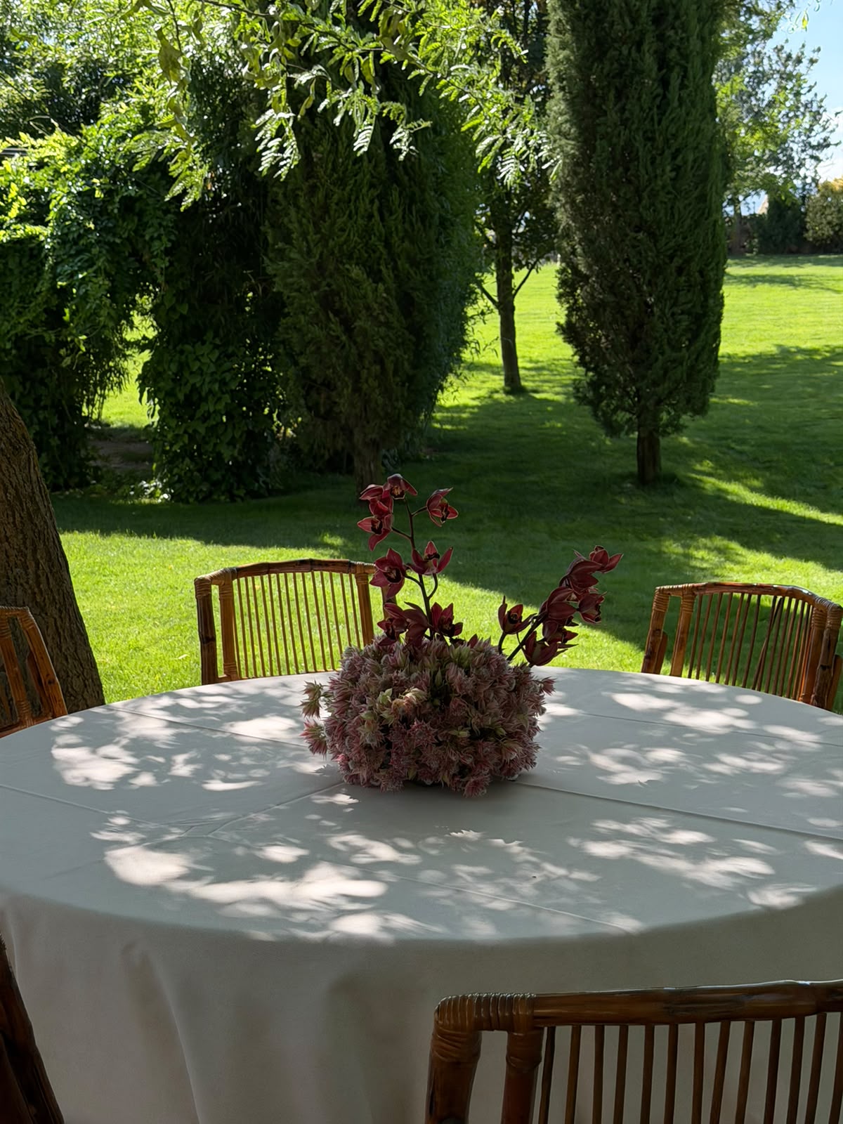 Centro floral en tonos rosa y burdeos sobre una mesa de boda al aire libre
