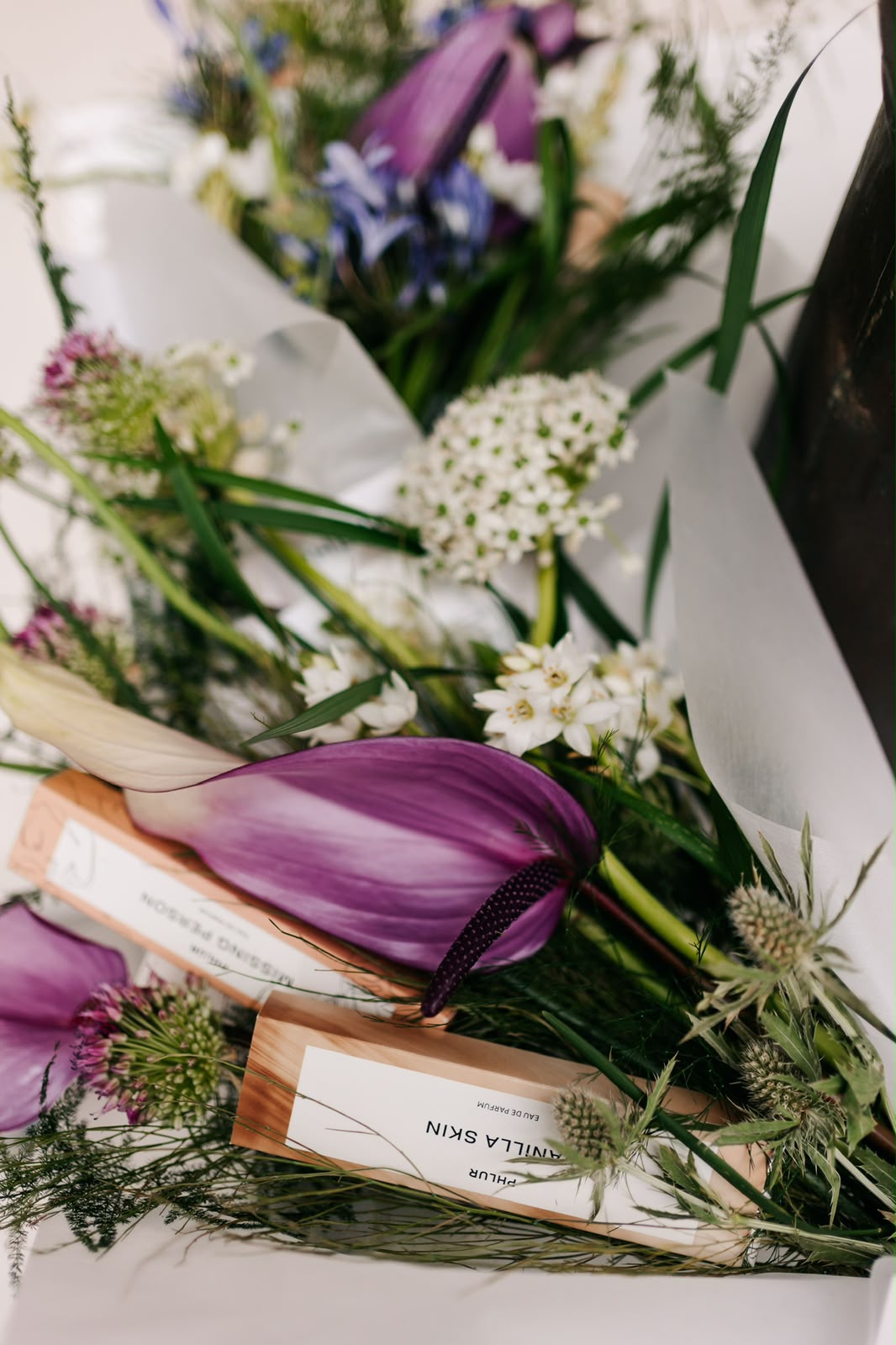 Detalle de flores moradas y blancas junto a muestras de perfume Phlur