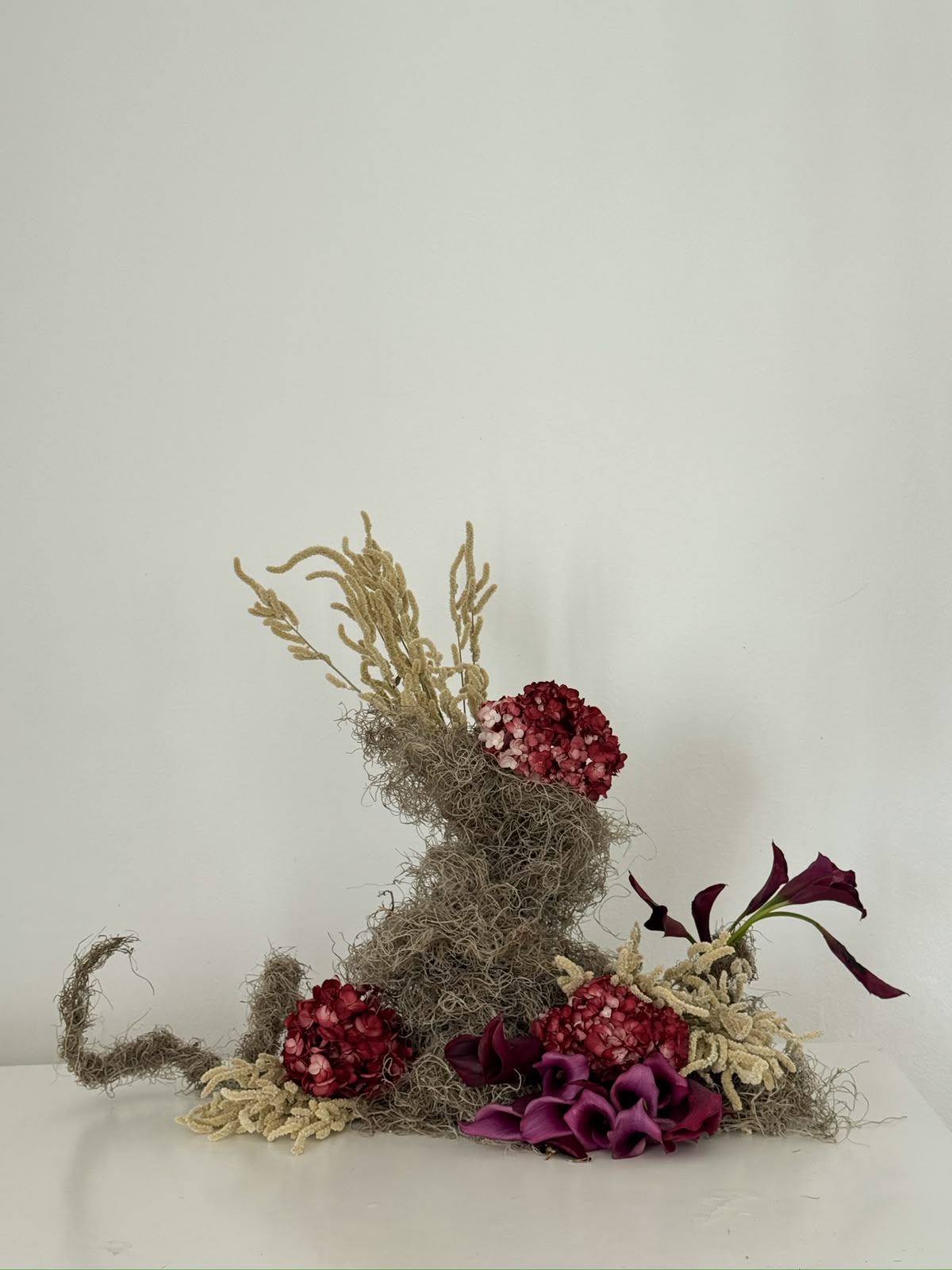 Pieza botánica escultórica con musgo gris, hortensias y calas color vino