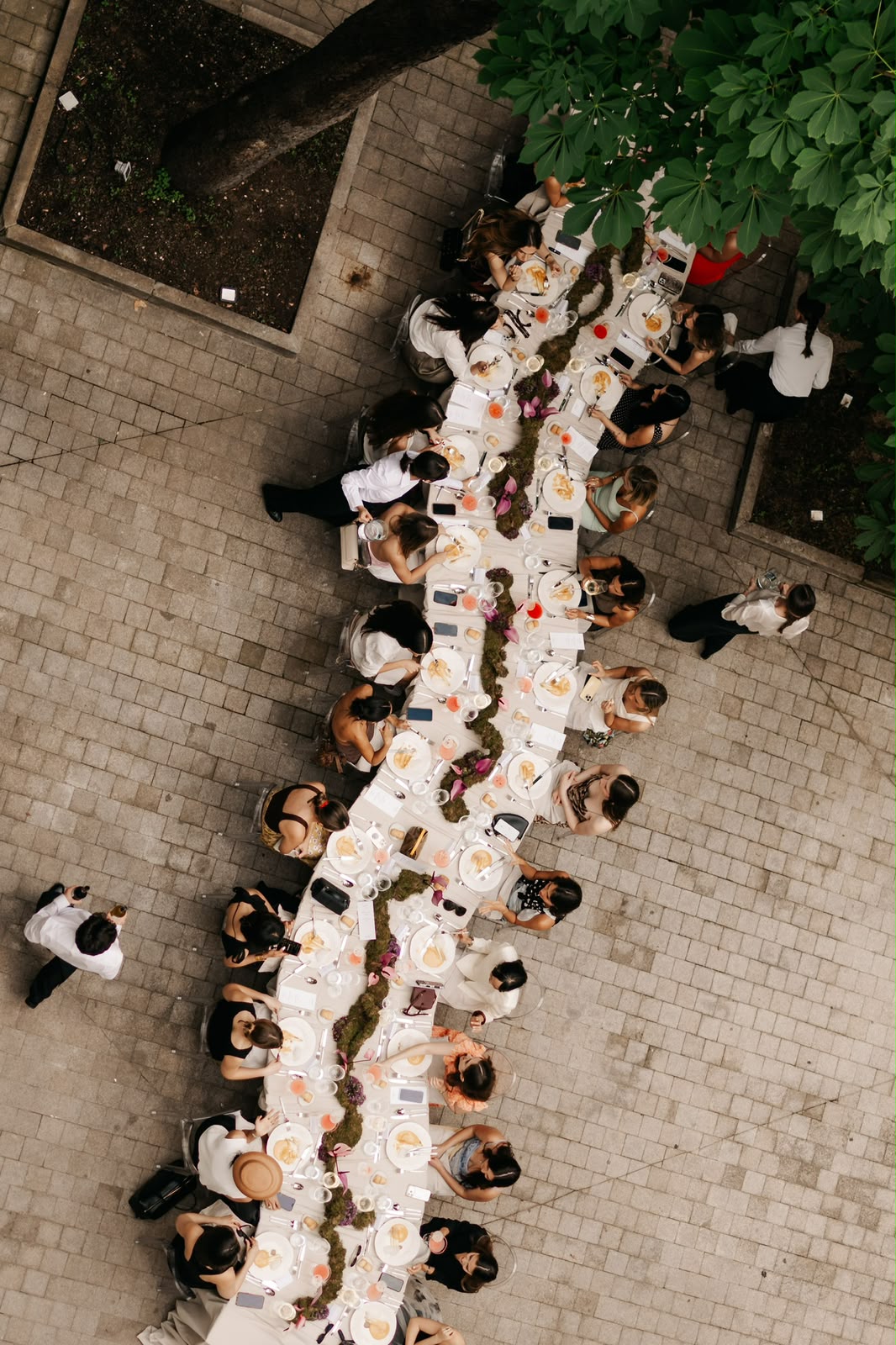 Vista cenital de una mesa larga con invitados y decoración botánica
