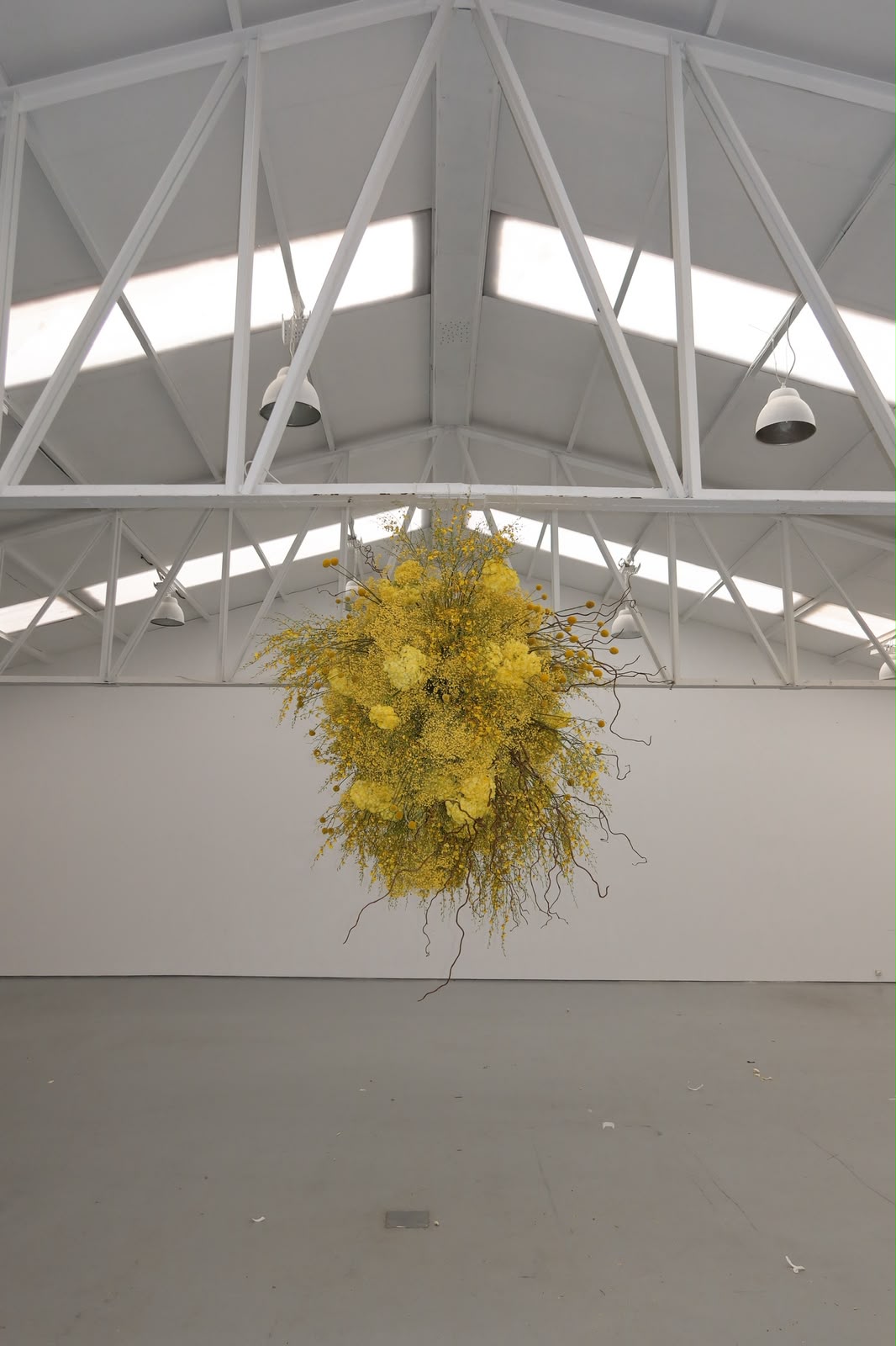 Gran instalación floral amarilla suspendida en una nave blanca